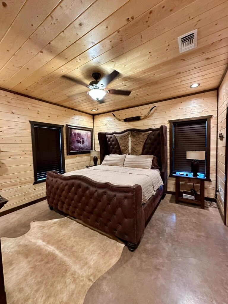 Bedroom suite with a tufted leather bed, longhorn mount, and cowhide rug